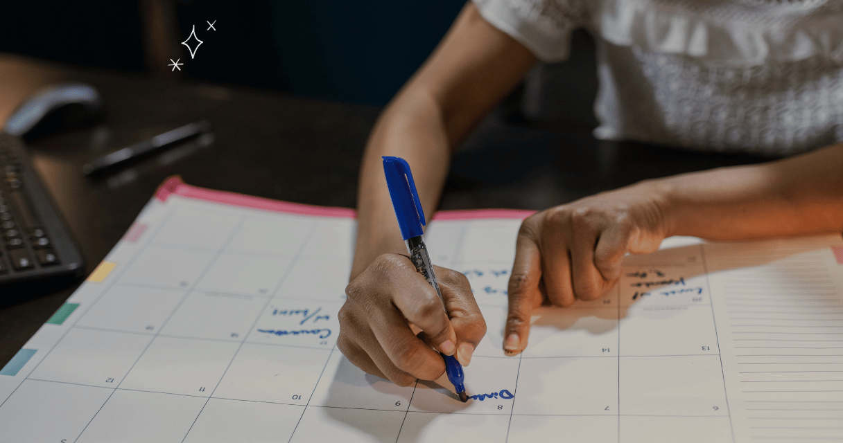 Person writing on a calendar with a blue pen at a desk, planning tasks for the holidays month.