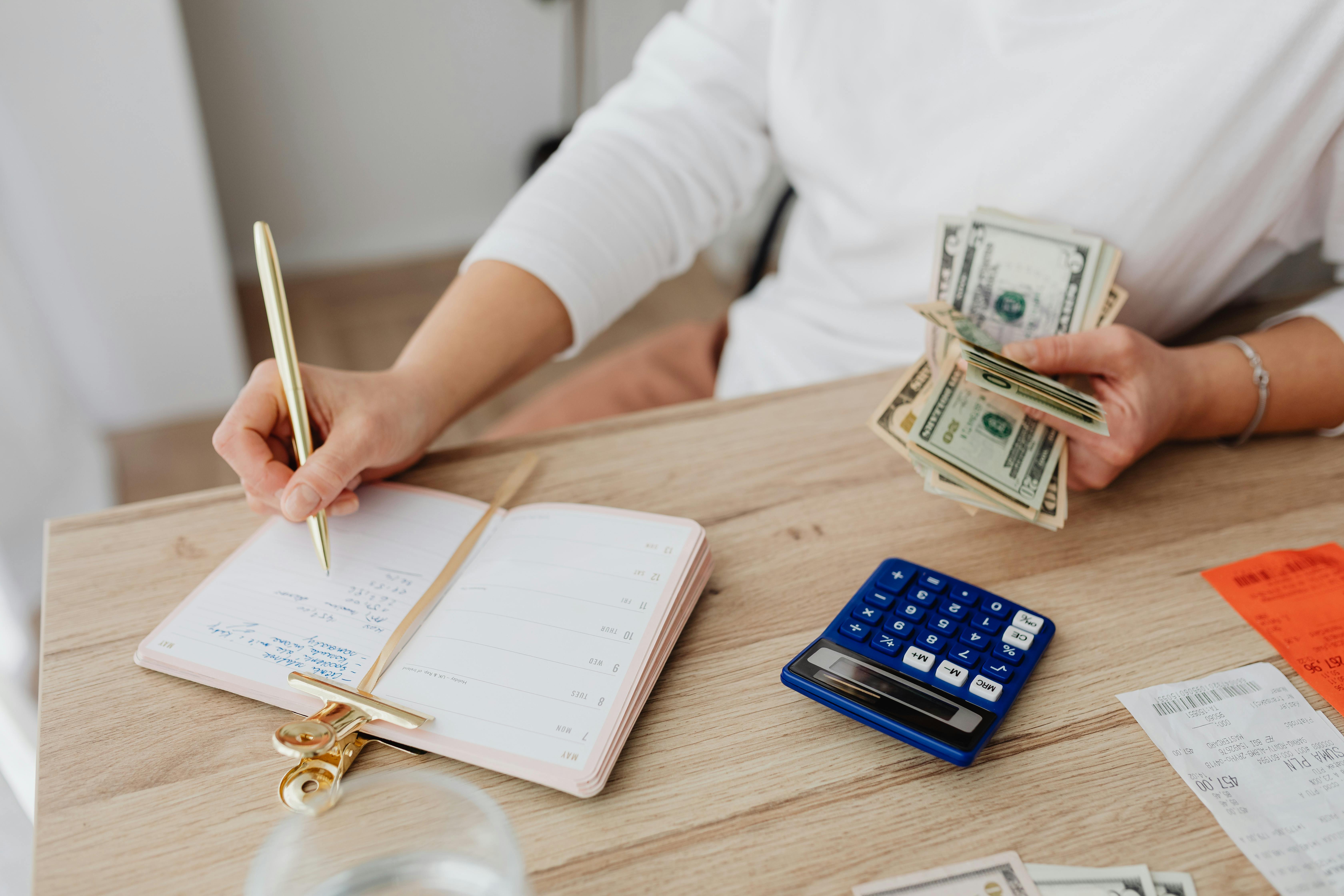 Person budgeting at a desk with cash, a calculator, and a notebook.