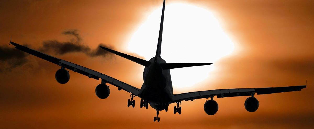 A silhouette of an airplane in flight against a dramatic orange sky, with the sun glowing brightly in the background, partially obscured by clouds that will make people Save Money 