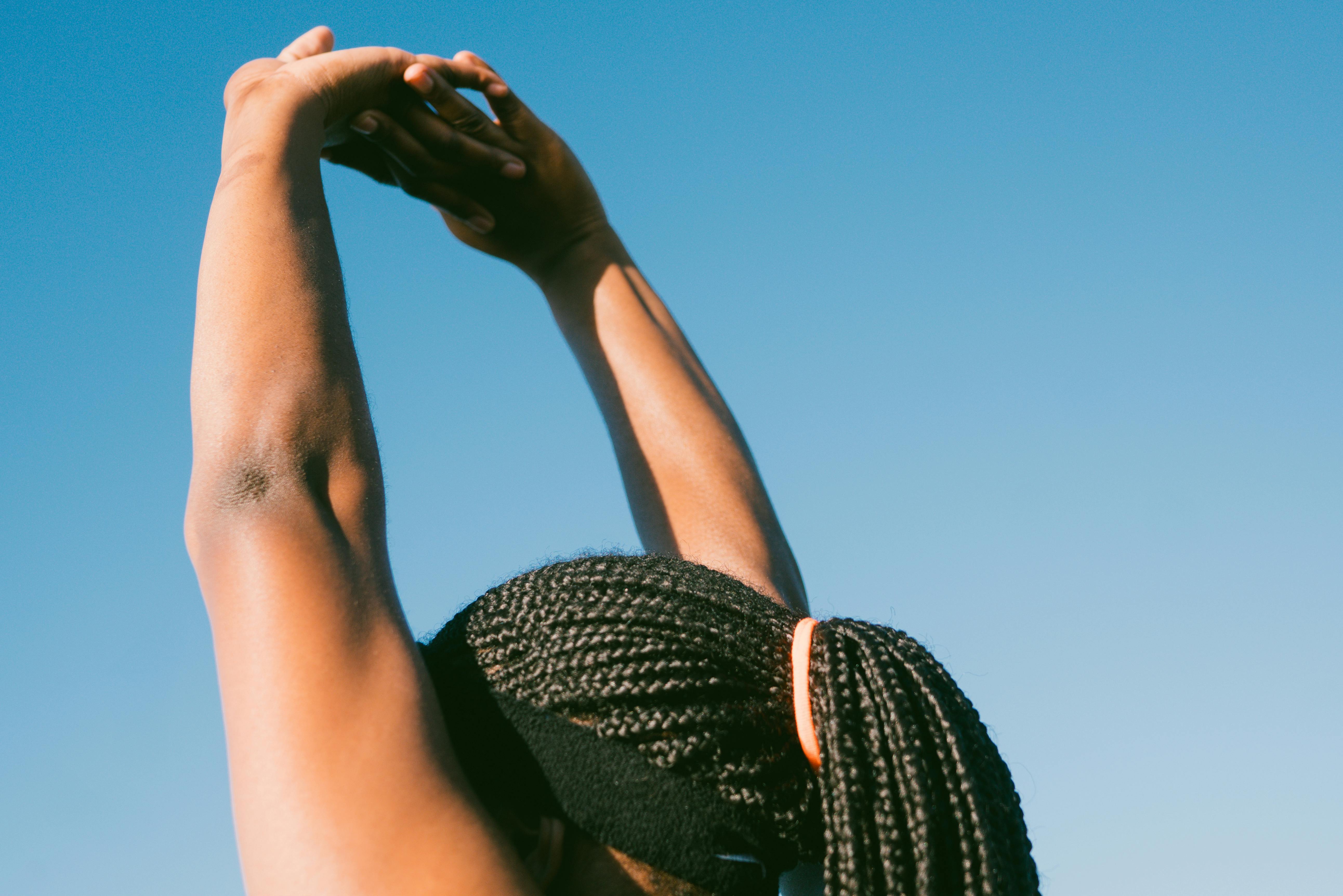 Person stretching outdoors with arms raised against a clear blue sky.