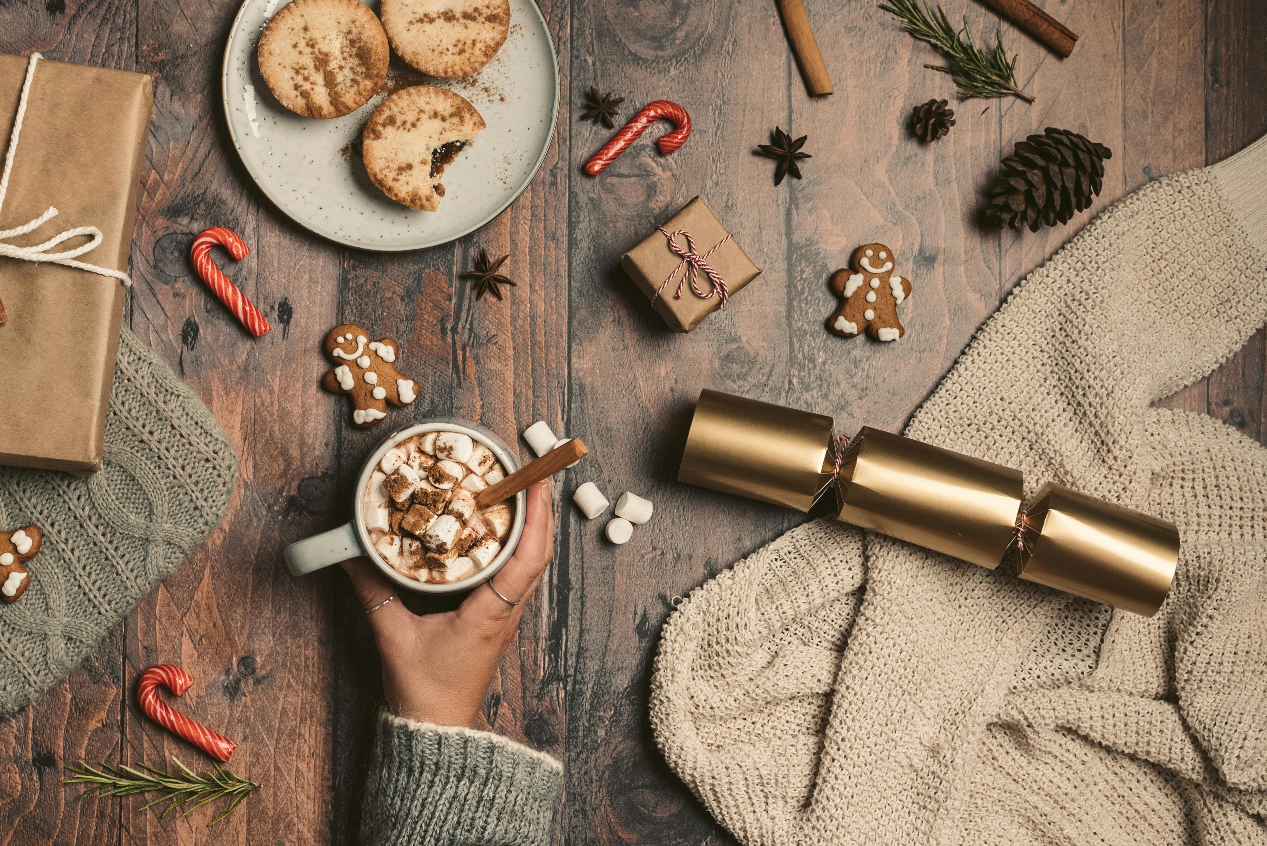 Festive holiday flat lay with cookies, hot chocolate, wrapped gifts, and decorations on a wooden table. Holiday tips to bring festivities to work.